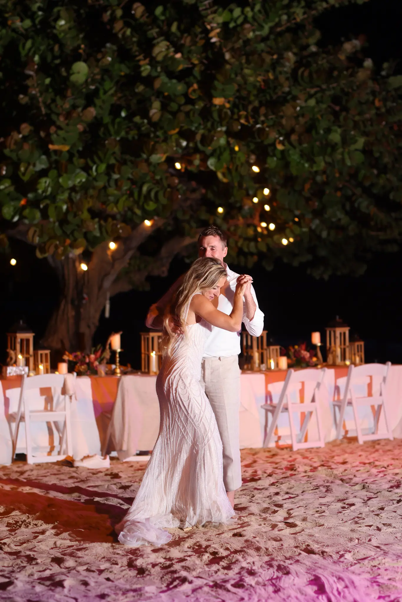 Bride and groom dancing outdoors beneath a tree and wedding reception lights