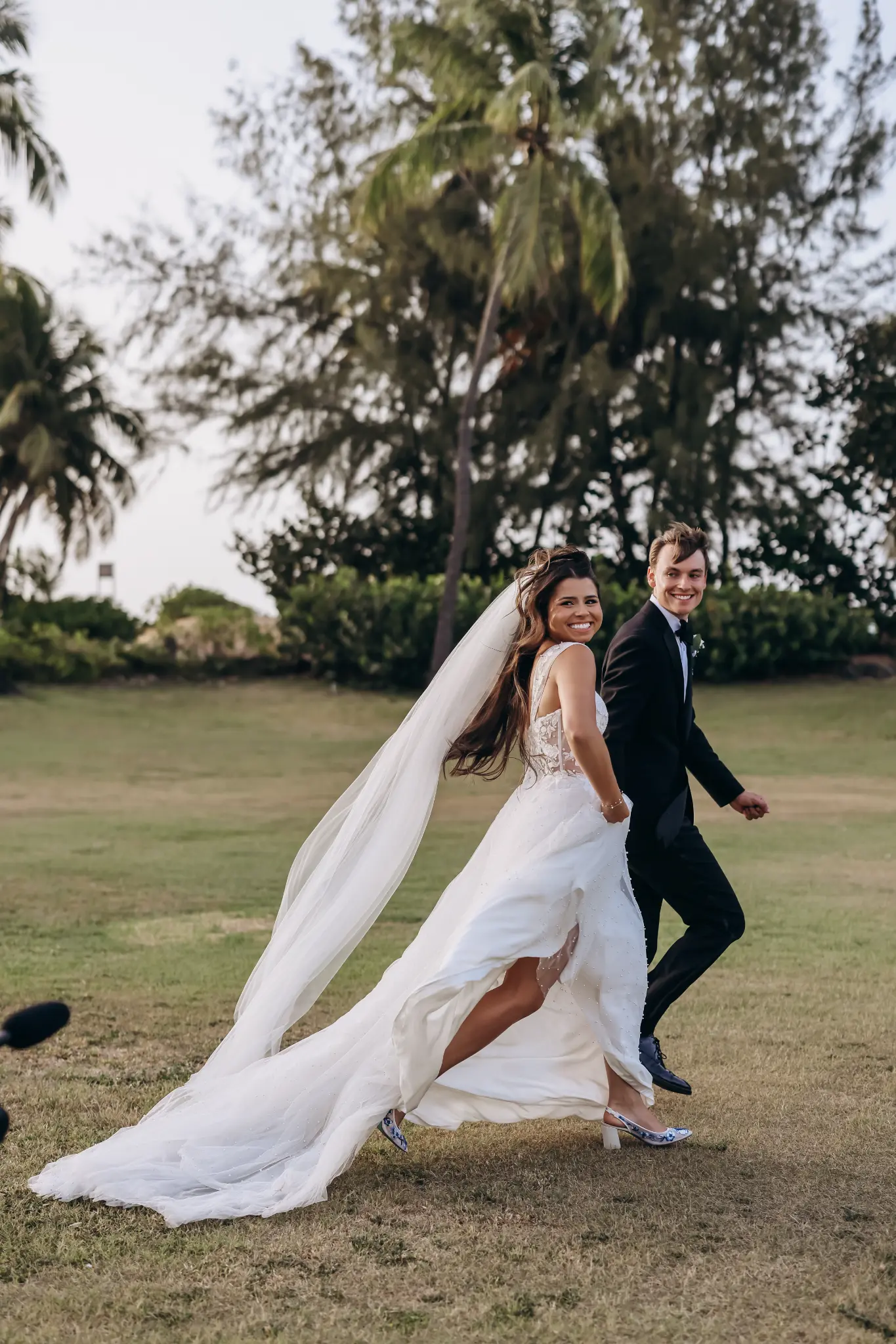 Bride and groom running together across a green field
