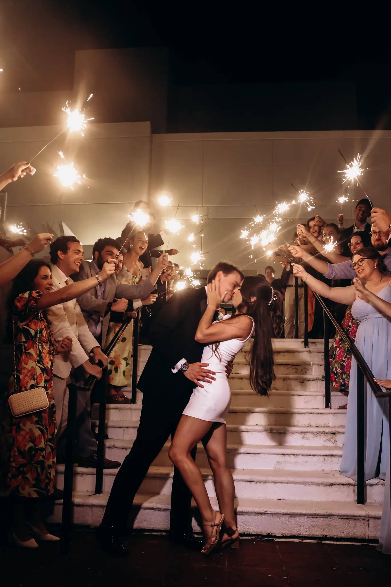 Wedding couple dancing among guests at a warmly lit reception staircase