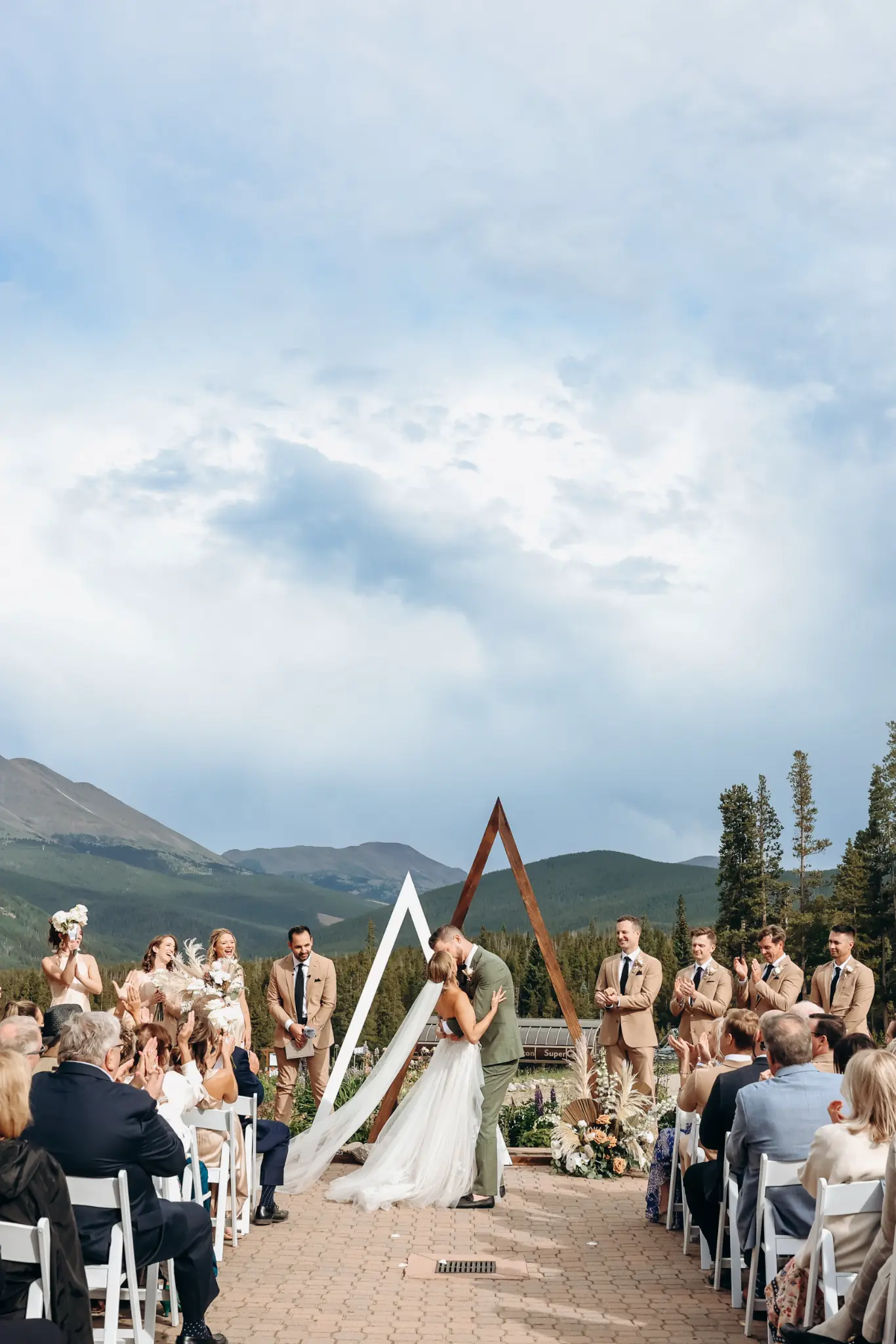 Couple kissing beneath a geometric outdoor ceremony arbor with mountains behind them