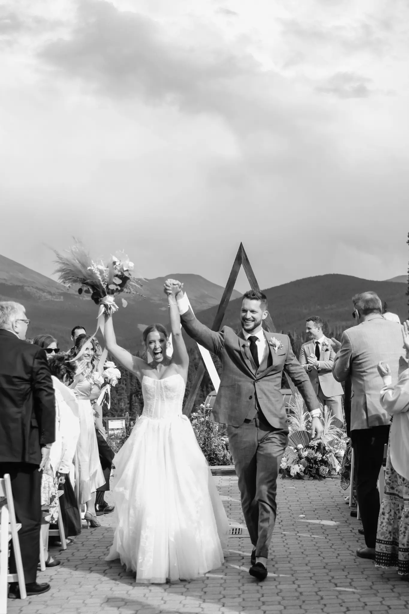 Black-and-white newly married couple celebrating during a mountain-view outdoor ceremony recessional