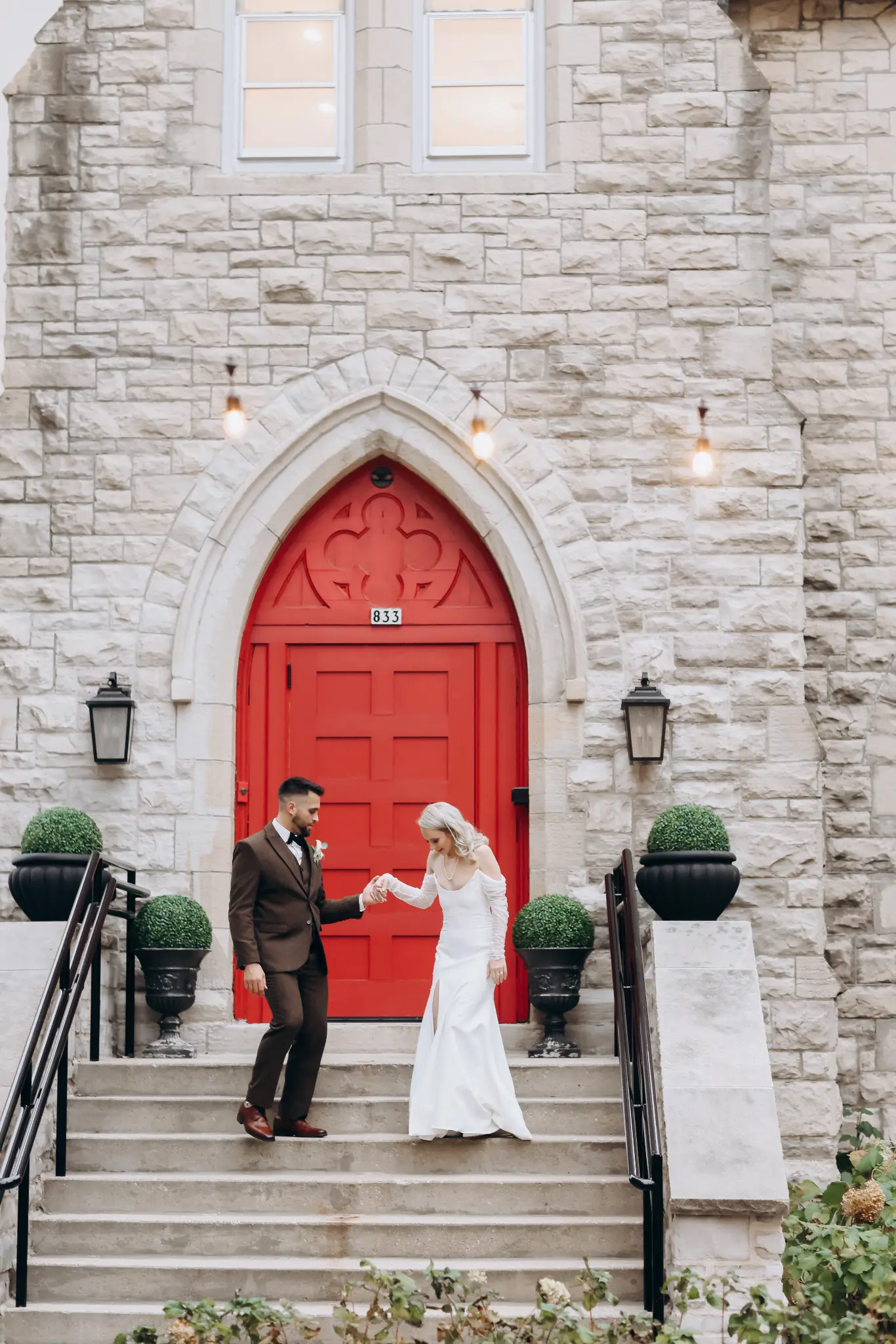 Bride and groom standing in front of red double doors at a stone building