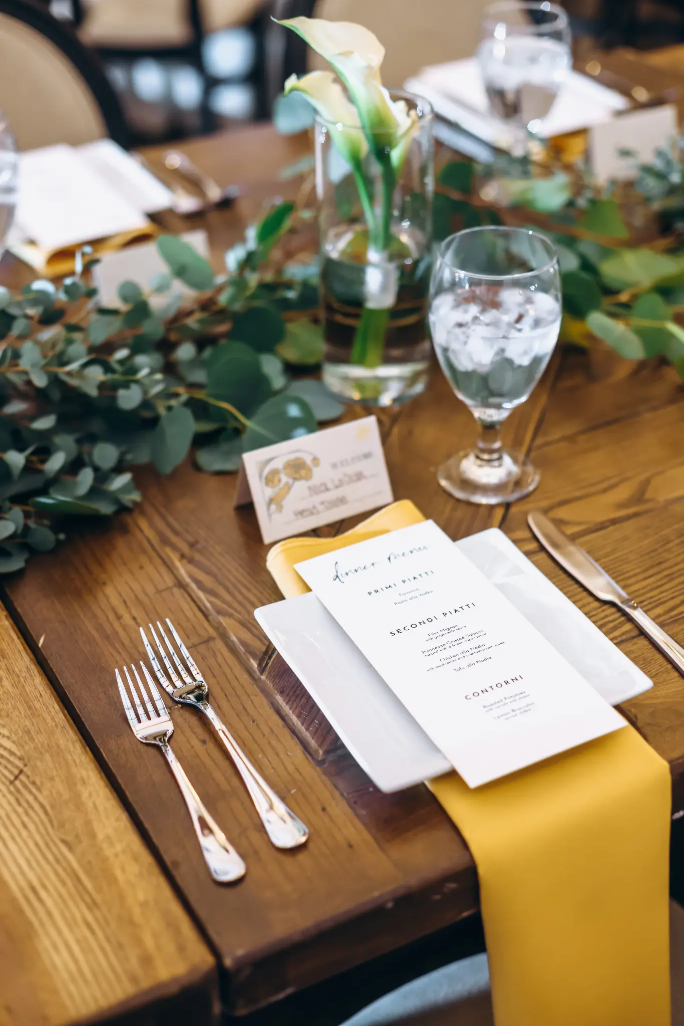 Wedding reception menu, place setting, greenery, and water glass on a table