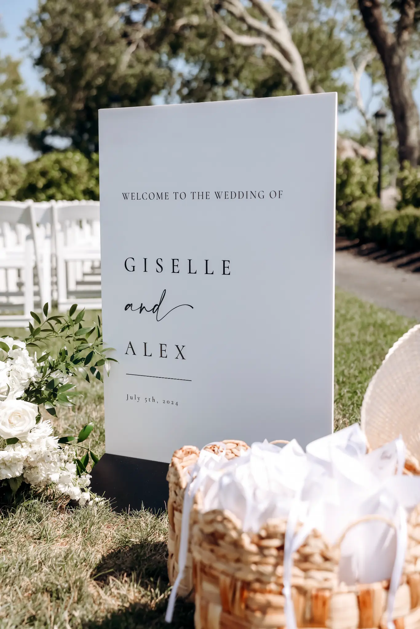 Wedding welcome sign framed by white flowers and baskets of ceremony fan favors