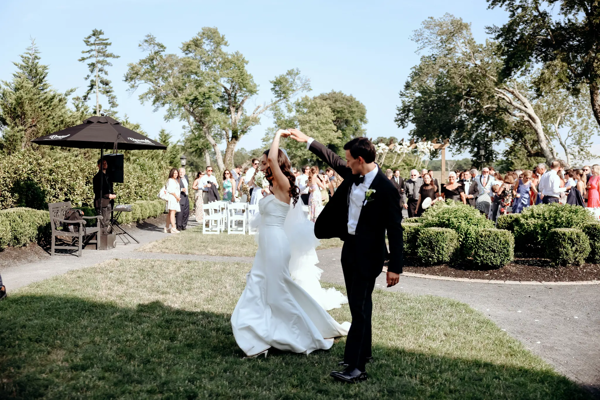 Newly married couple spinning together on a garden lawn as guests gather after the ceremony