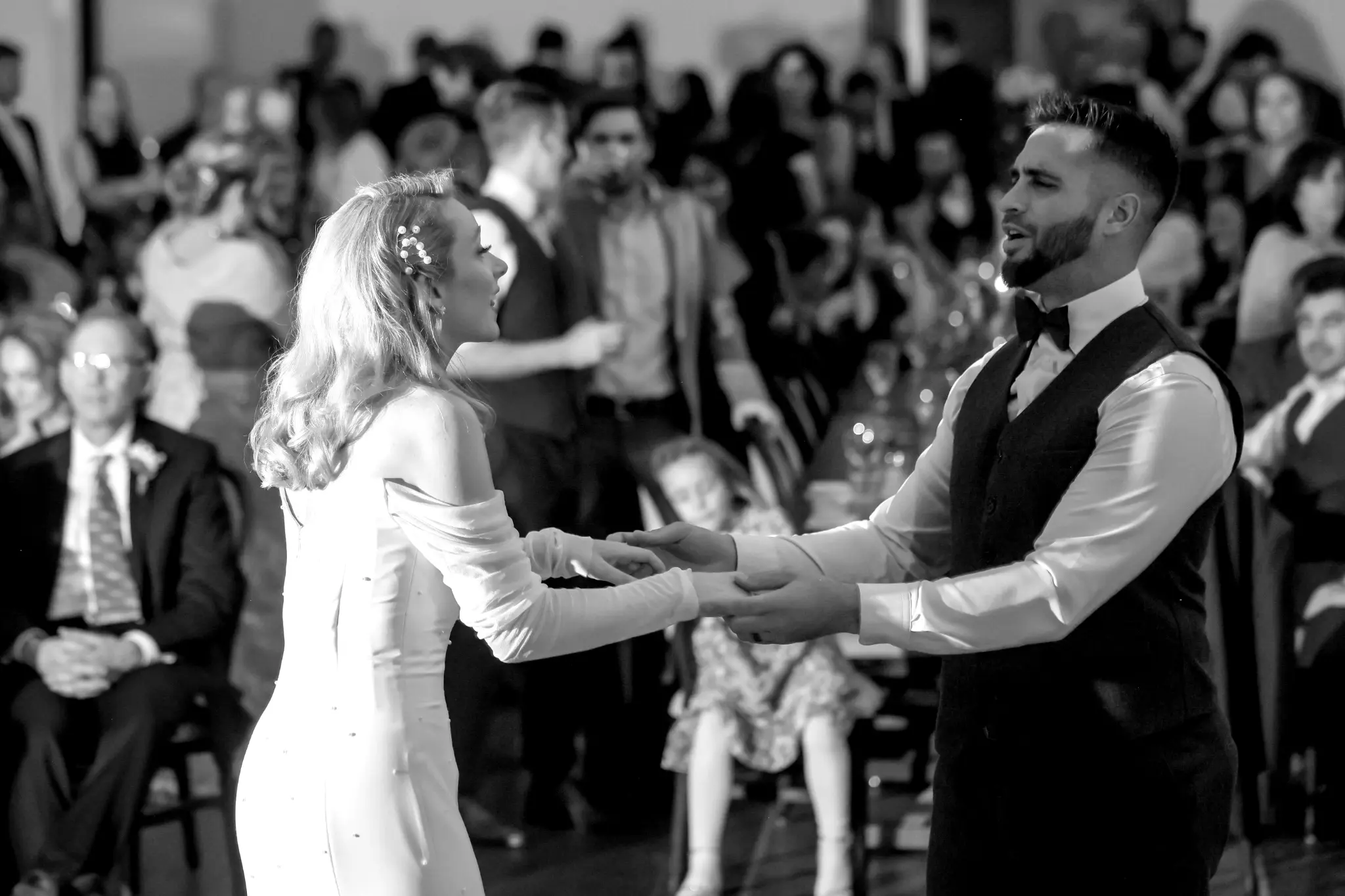 Black-and-white first dance with wedding guests gathered behind the bride and groom
