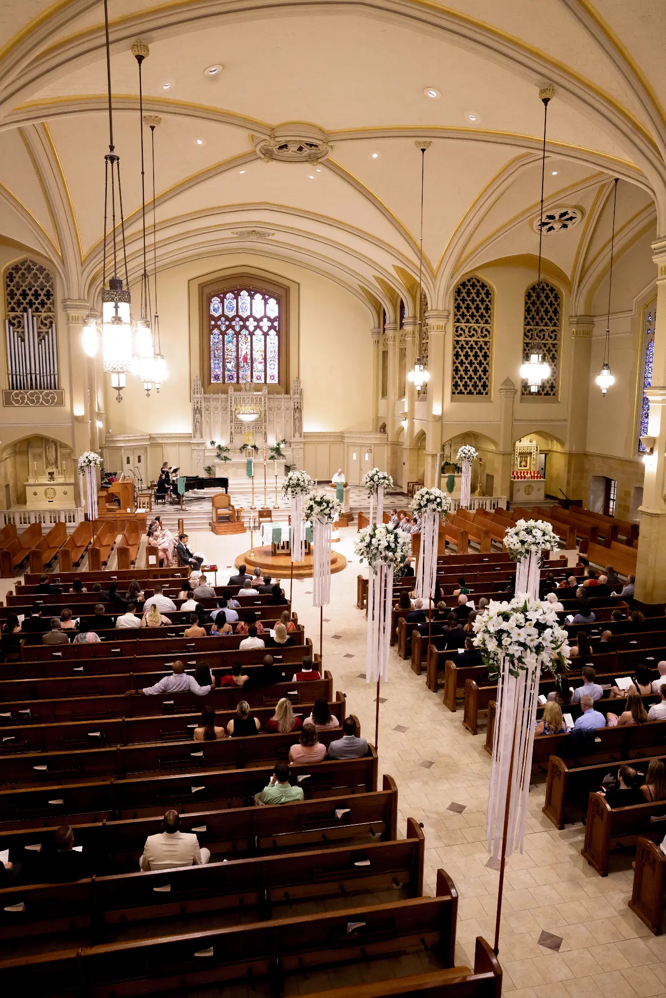Elevated view of a candlelit church ceremony with floral aisle arrangements, stained glass, and guests in pews
