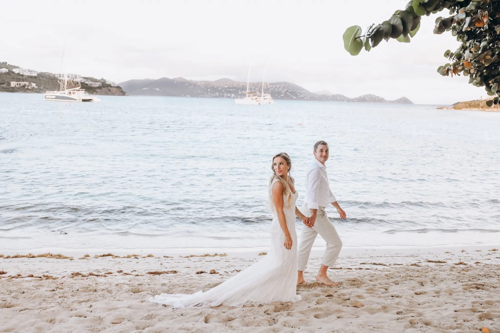 Bride and groom walking on a sandy beach by calm water