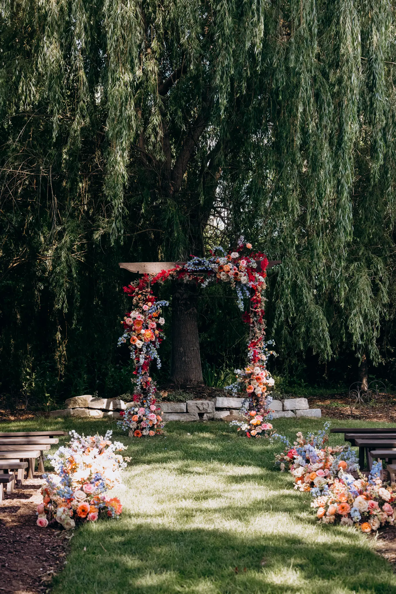 Flowered ceremony arbor and aisle beneath a mature weeping tree before guests arrive