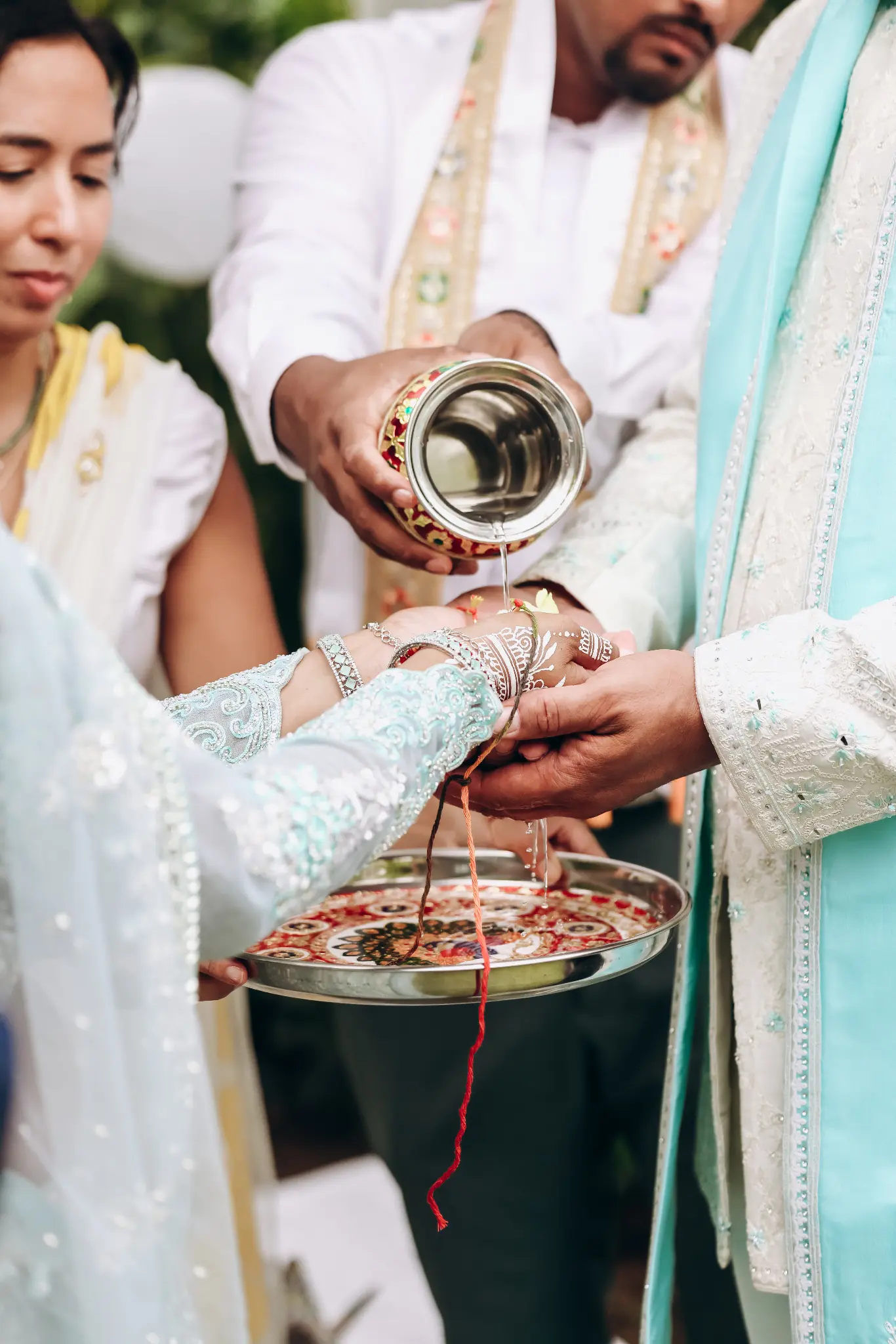 Close-up wedding ritual with water poured over joined hands connected by a red thread