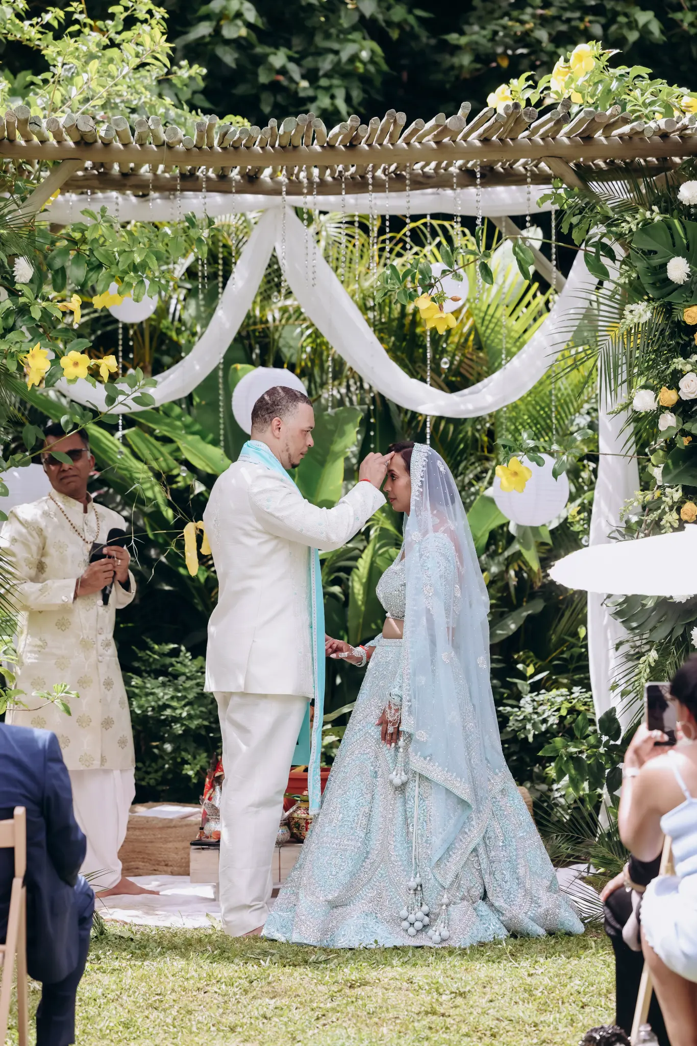 Couple participating in a South Asian wedding ritual beneath a draped flowered outdoor canopy