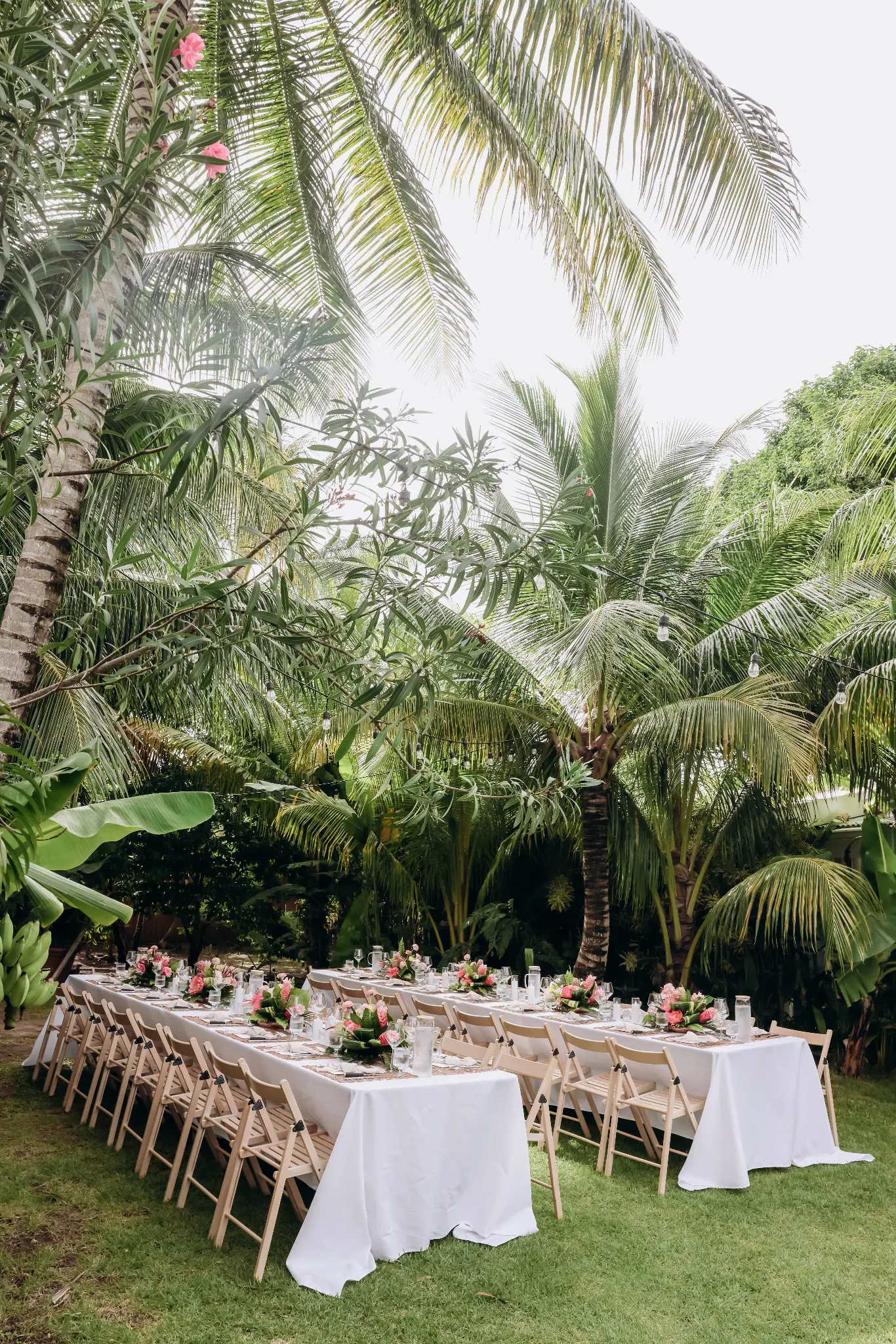 Long outdoor wedding dinner tables set in a tropical landscape