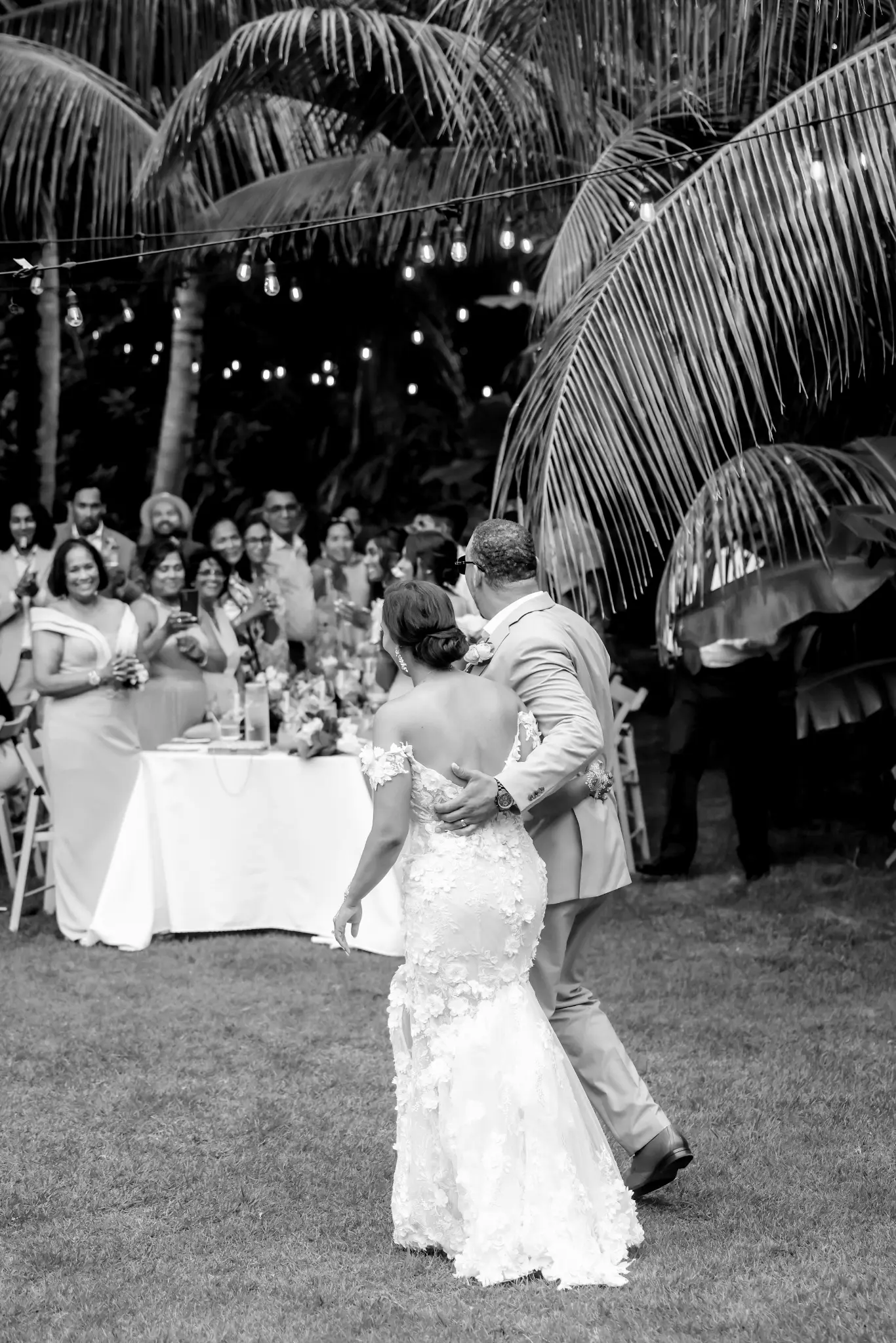Bride and groom dancing outdoors at night while wedding guests look on