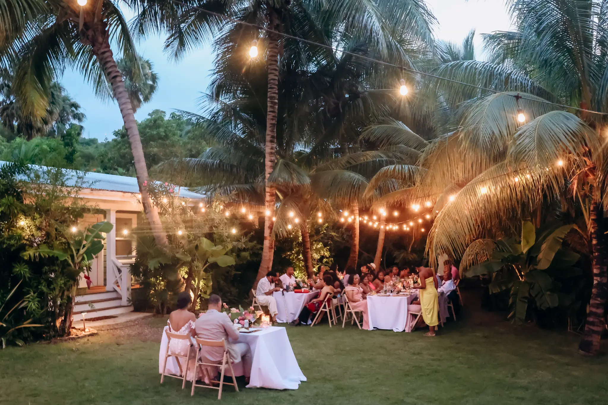 Outdoor wedding reception tables beneath palms and string lights
