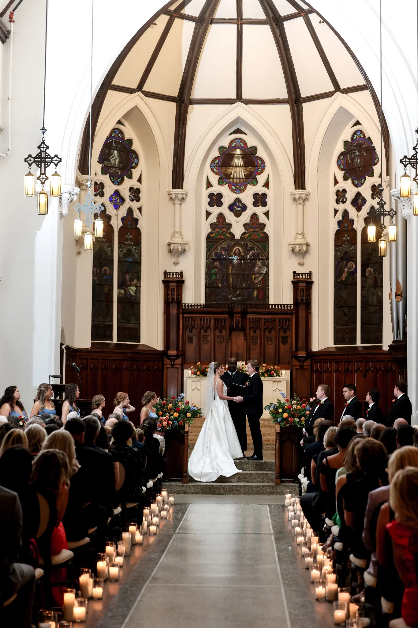 Couple exchanging vows in a candle-lined church aisle beneath stained-glass windows