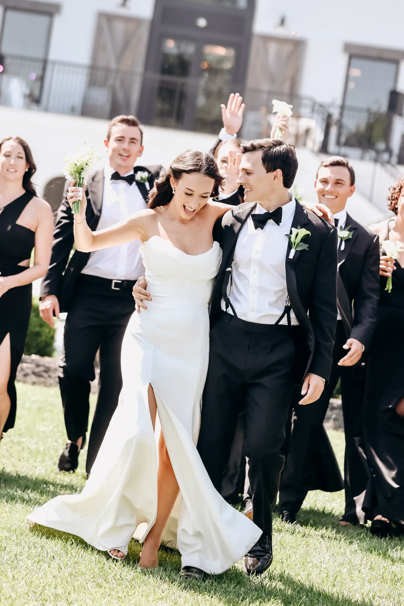 Bride and groom walking in front of a lively outdoor wedding party
