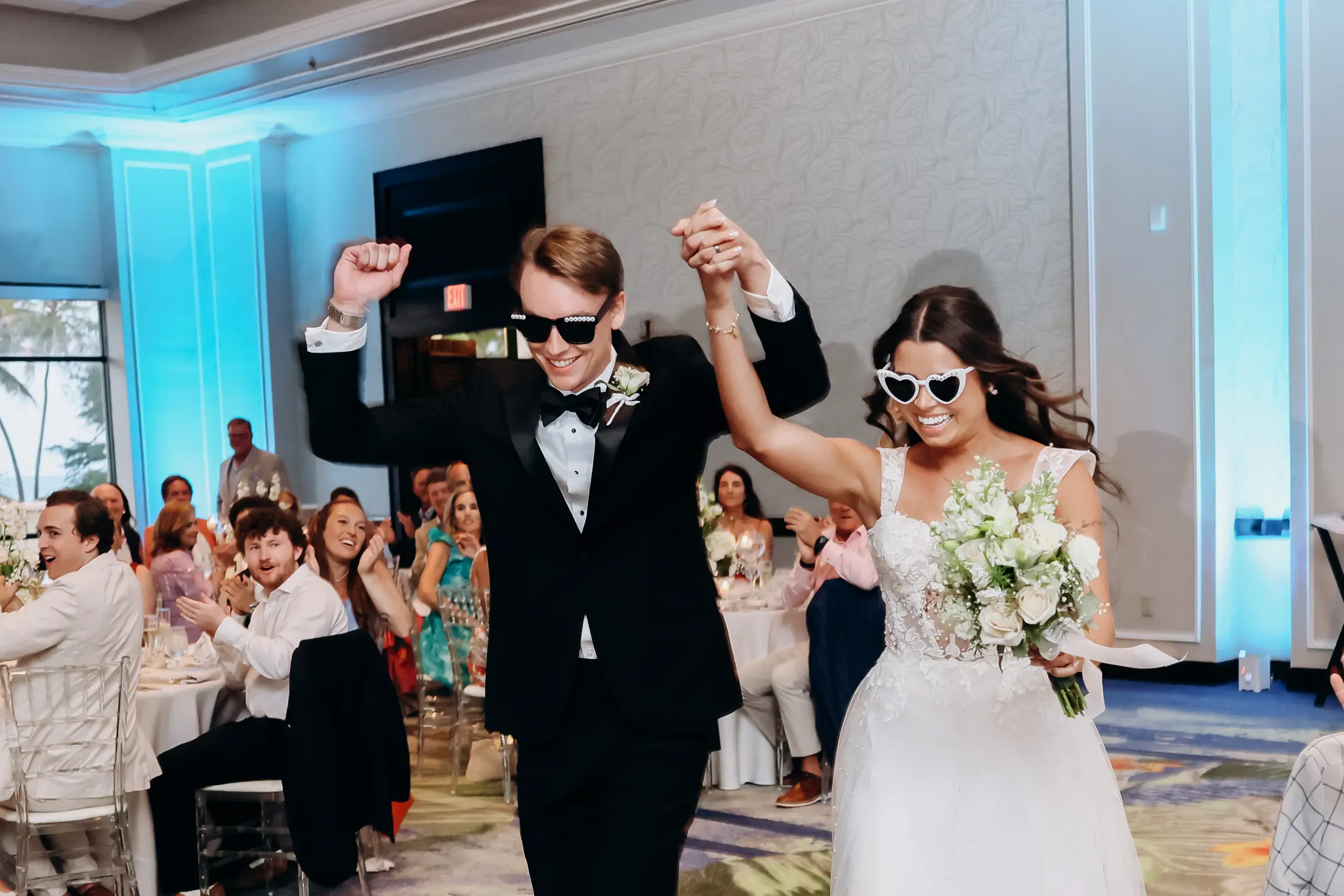 Bride and groom entering a bright wedding reception with their hands raised together