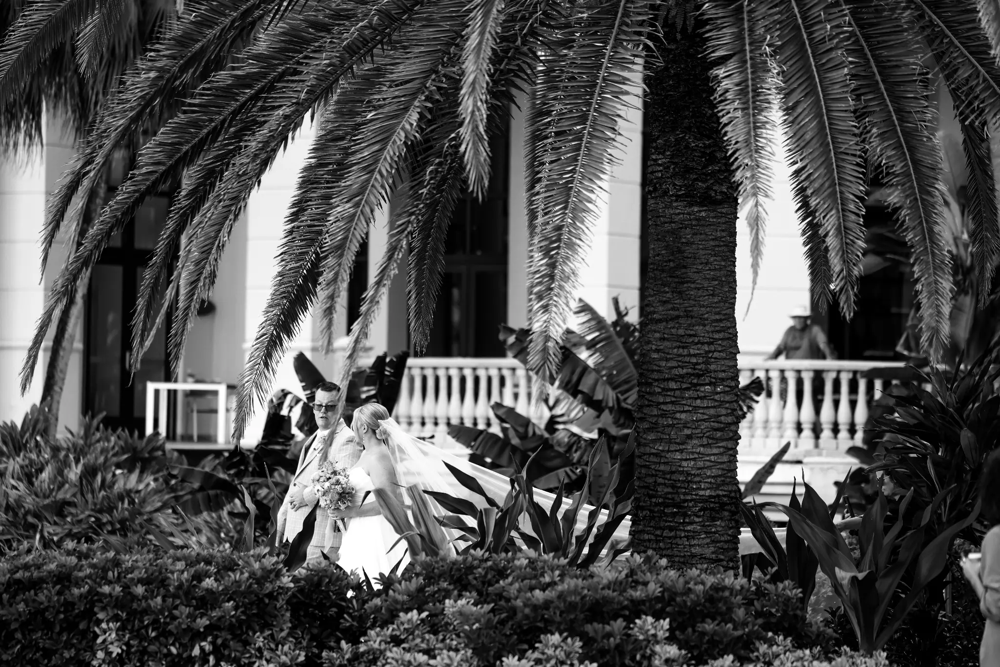 Black-and-white bride walking with an escort through a palm-lined garden before the ceremony