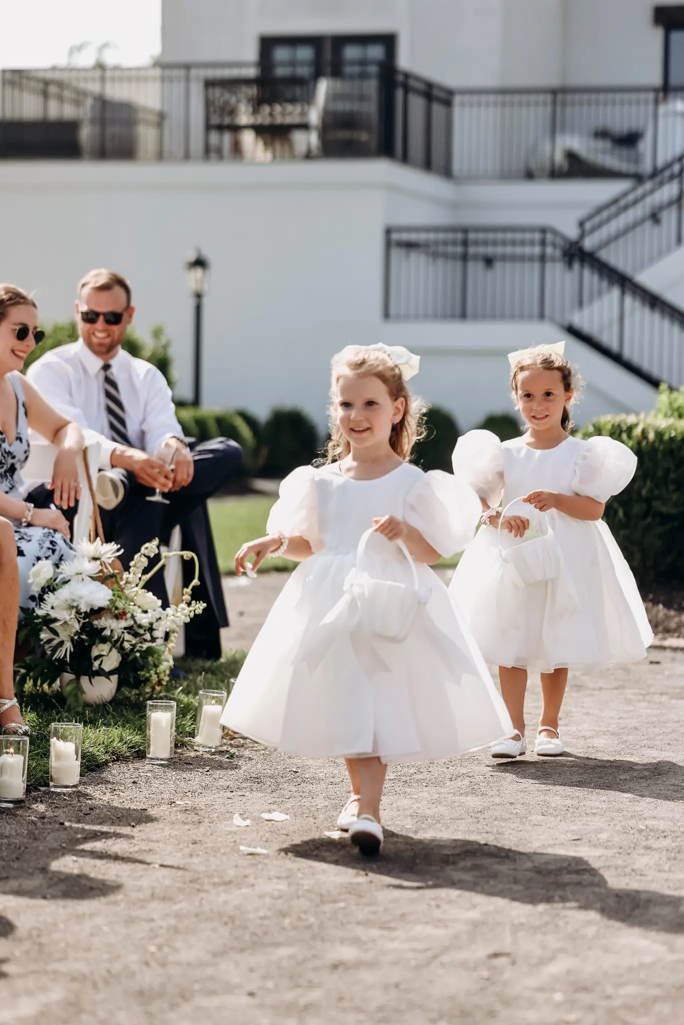 Two flower girls walking down an outdoor wedding aisle in white dresses