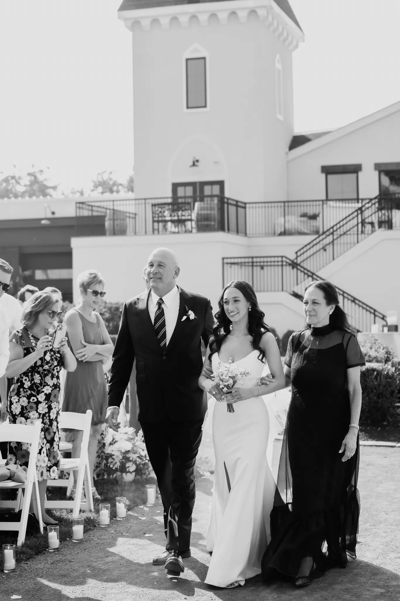 Black-and-white bride processional with two escorts along an outdoor aisle