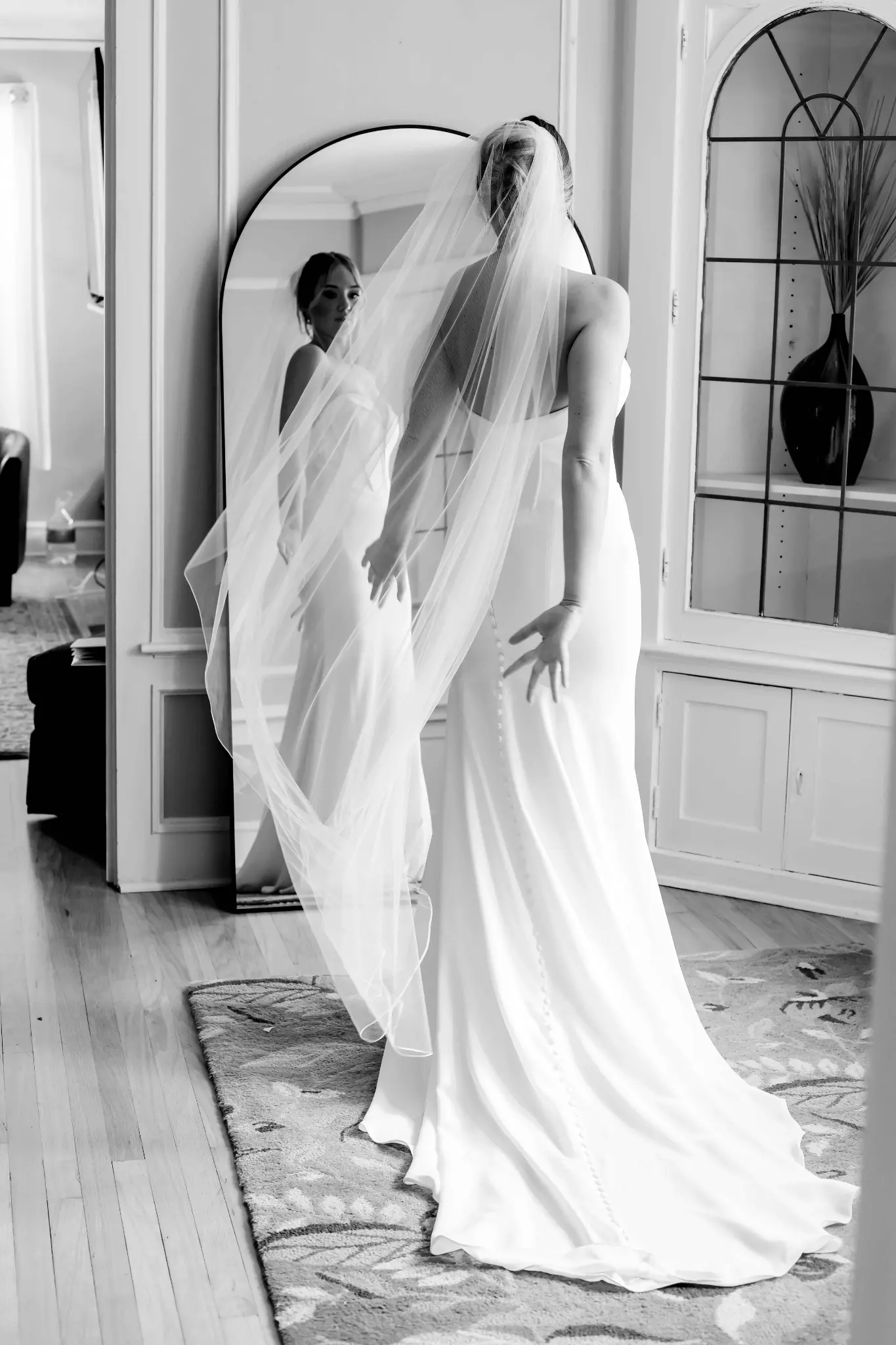 Black-and-white full-length bridal portrait reflected in a mirror during preparation