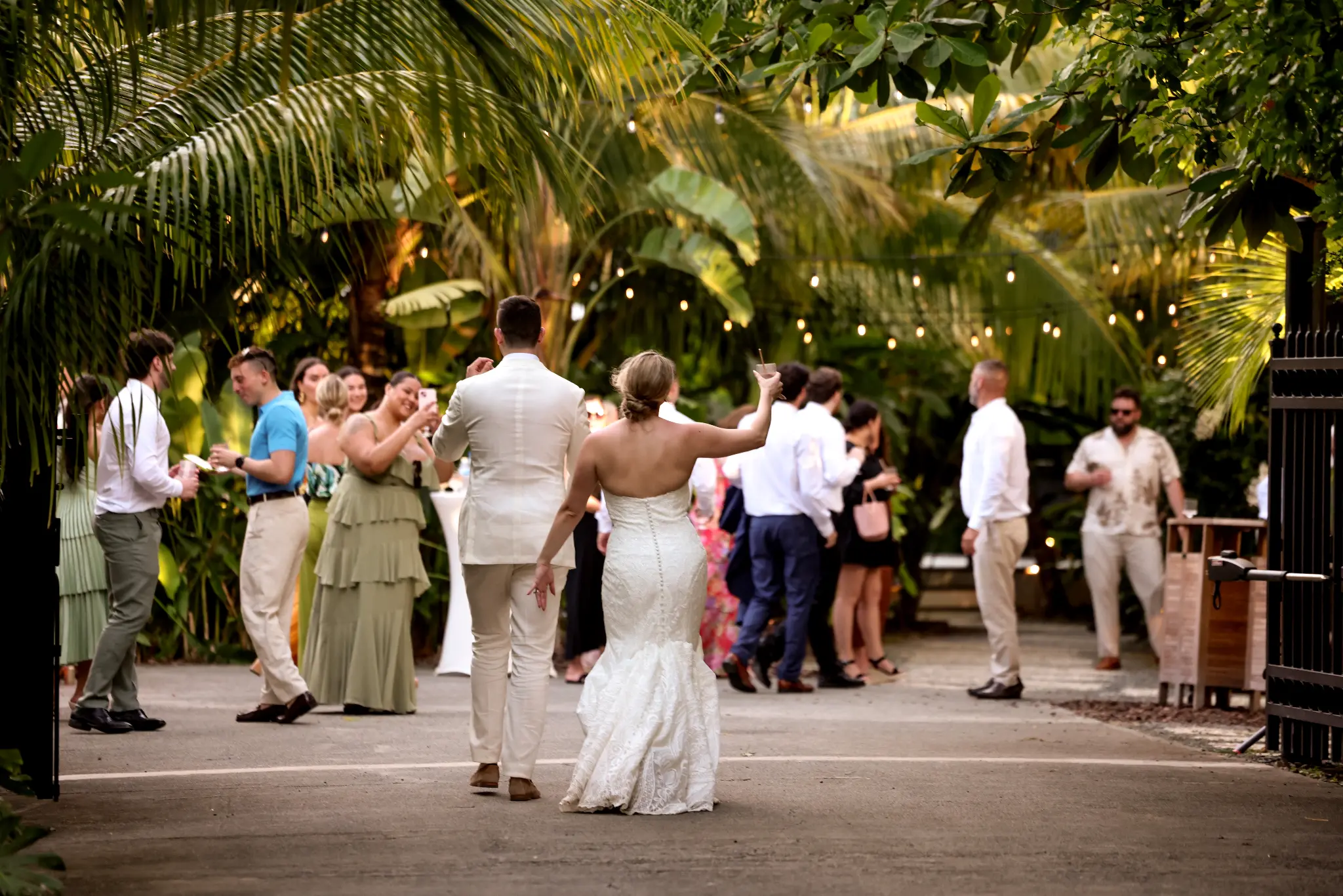 Bride and groom dancing outdoors as wedding guests gather beneath palms