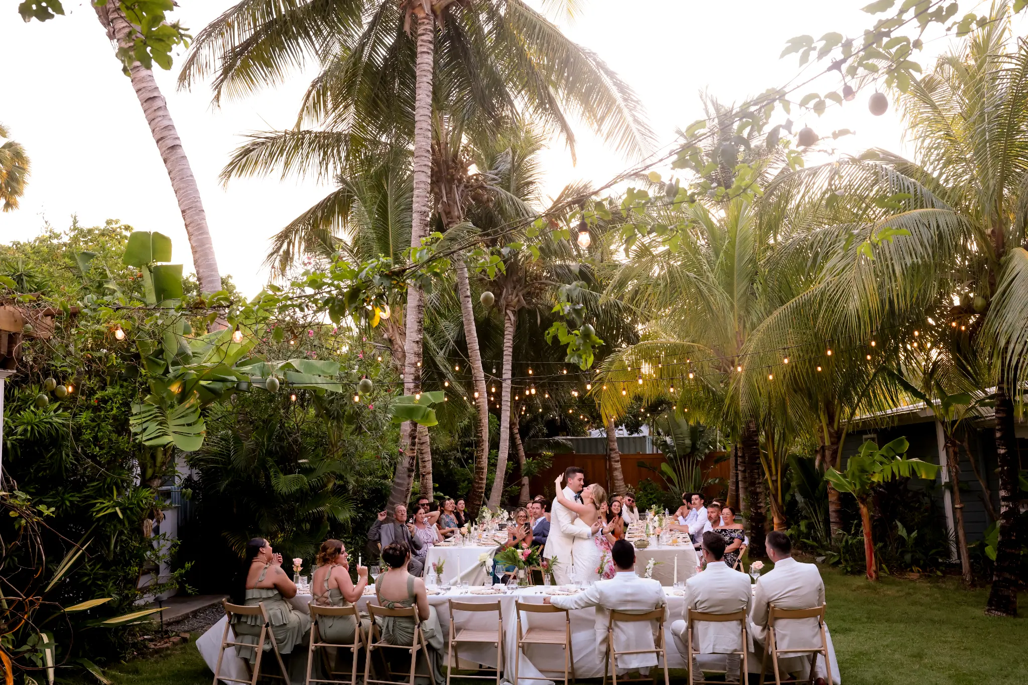 Long outdoor wedding reception table filled with guests in a tropical garden