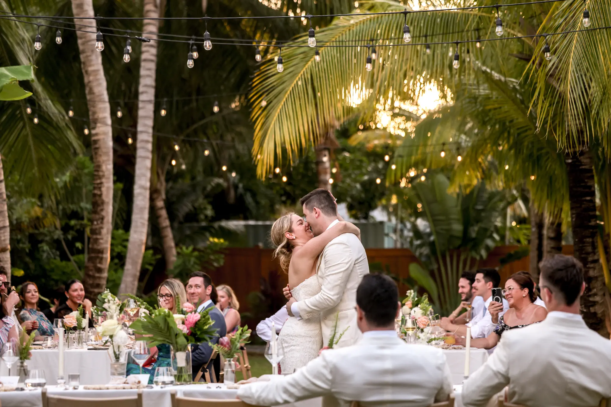 Bride and groom dancing outdoors with wedding guests seated at tables behind them