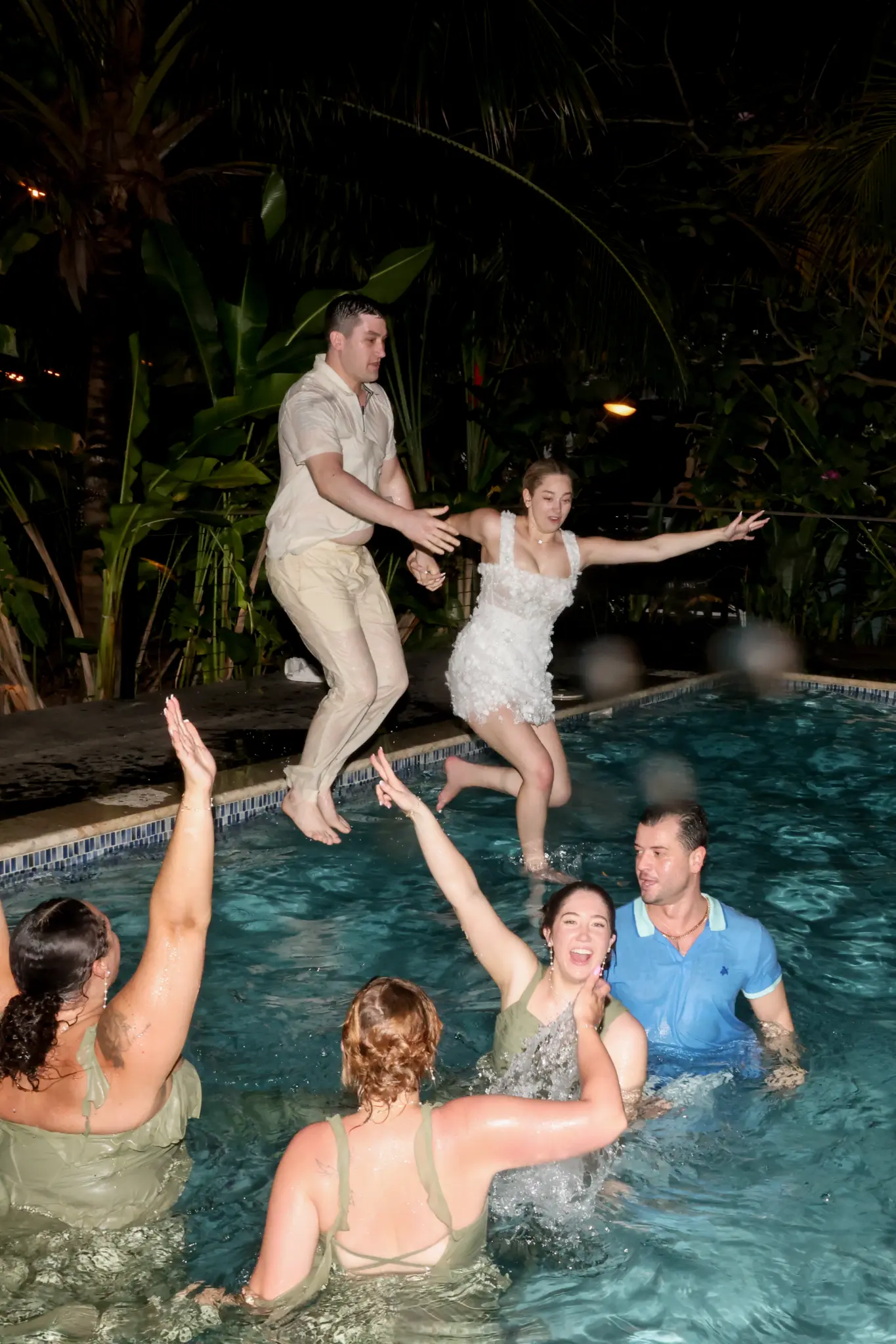 Wedding guests celebrating together in a swimming pool at night