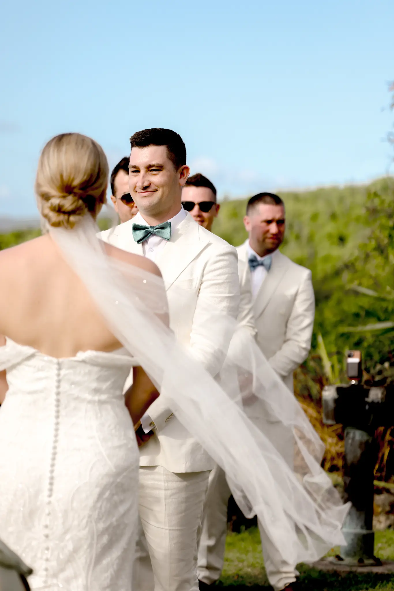 Groom reacting as a veiled bride reaches him at an outdoor ceremony altar