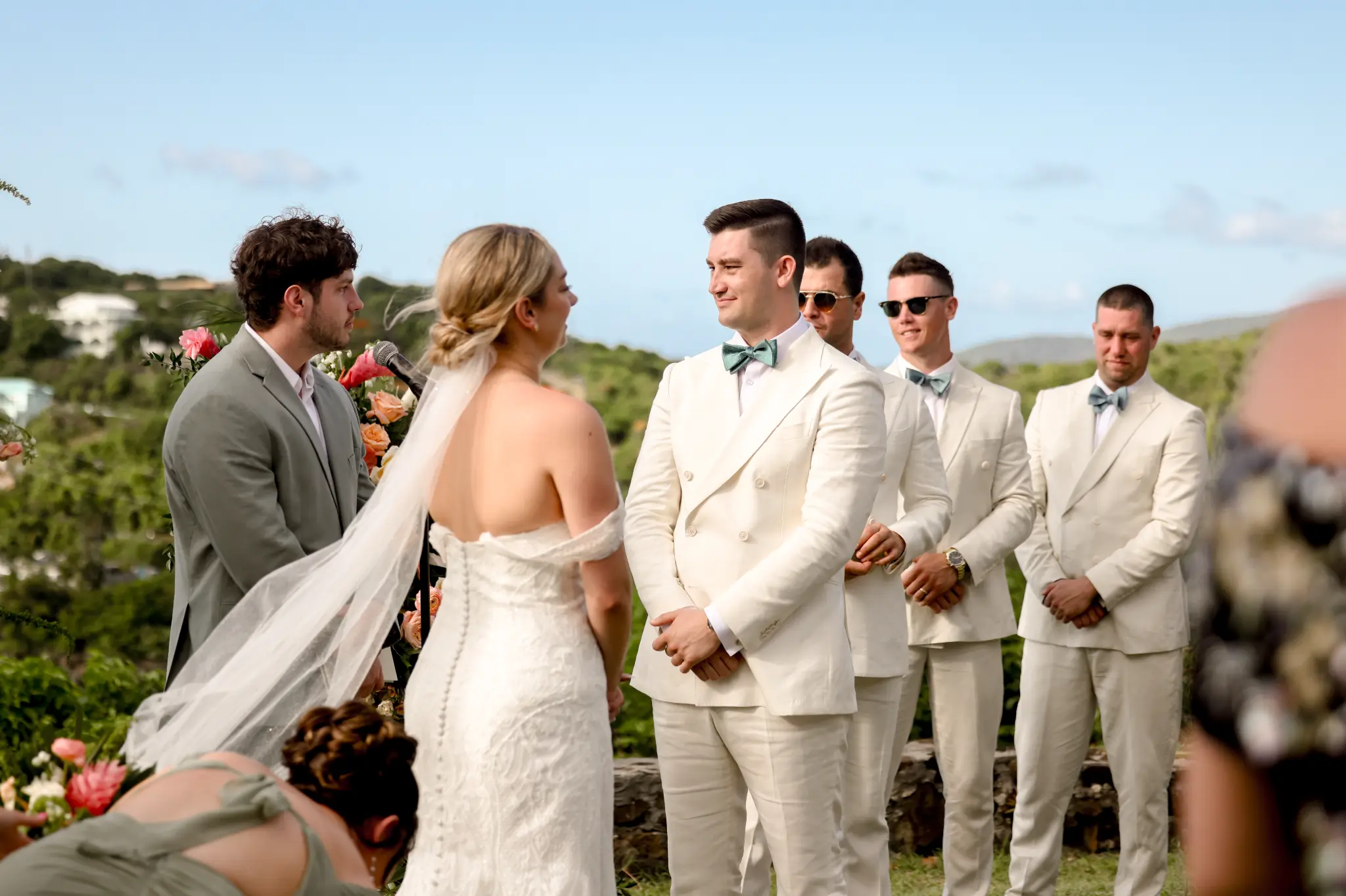 Bride and groom exchanging vows at an elevated outdoor wedding ceremony with attendants behind them
