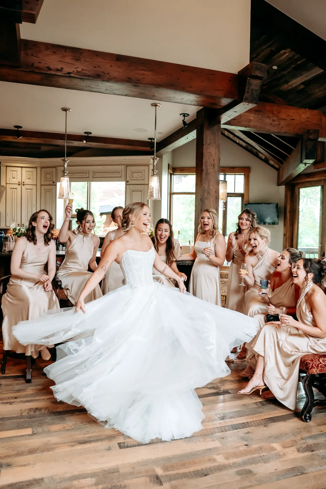 Bride spinning in her wedding gown while friends celebrate in a warm timbered room