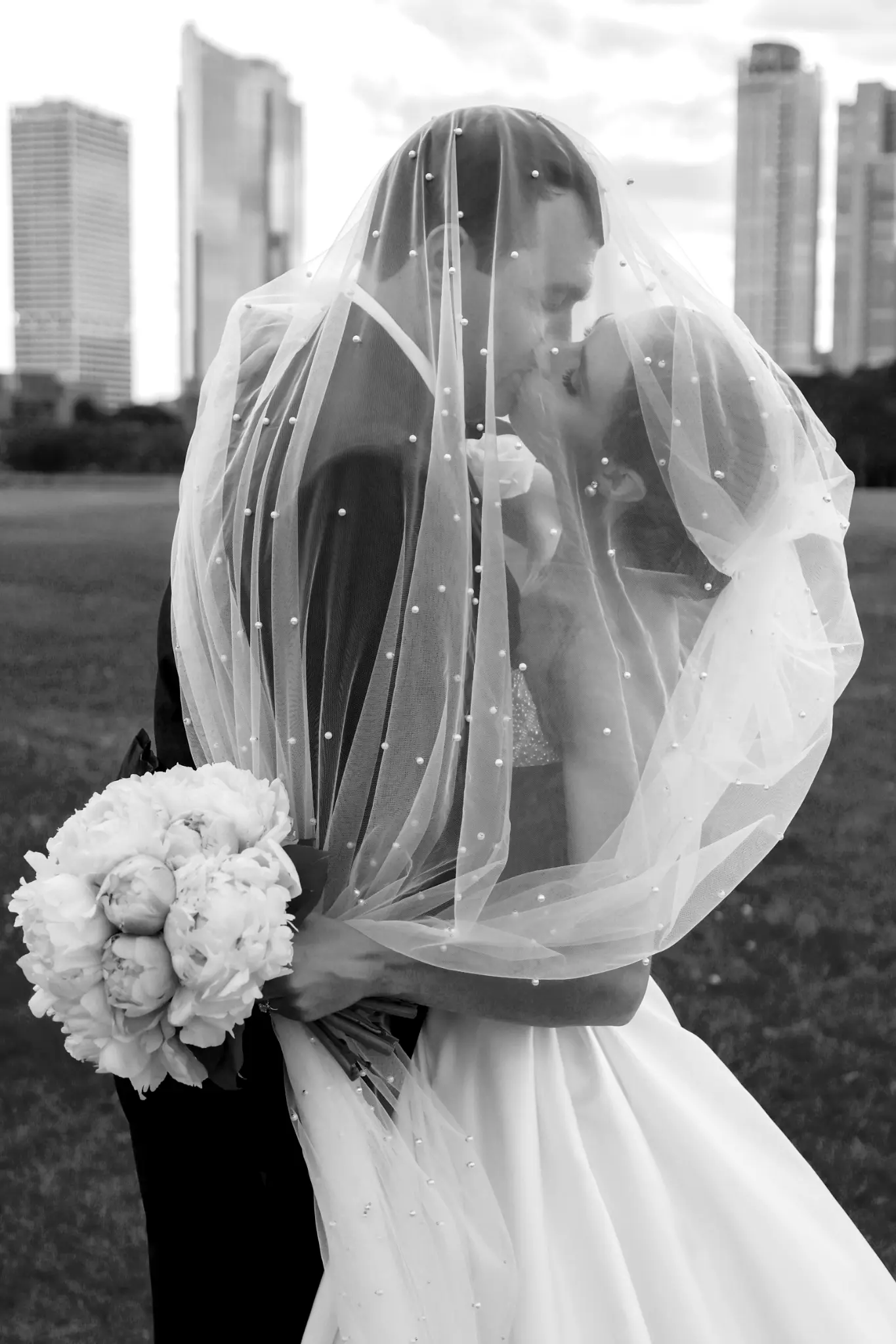 Black-and-white veiled bridal portrait near a city skyline