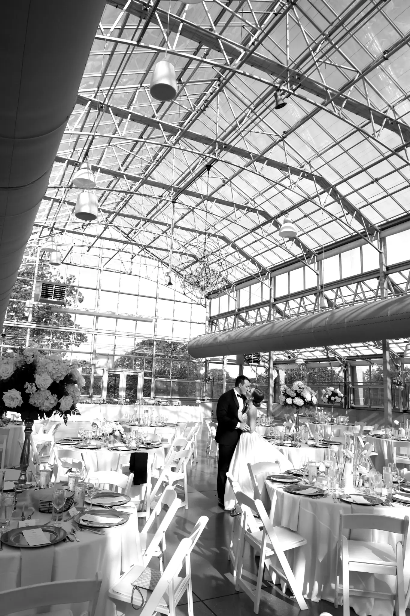 Black-and-white overview of an industrial glass wedding reception space with tables set