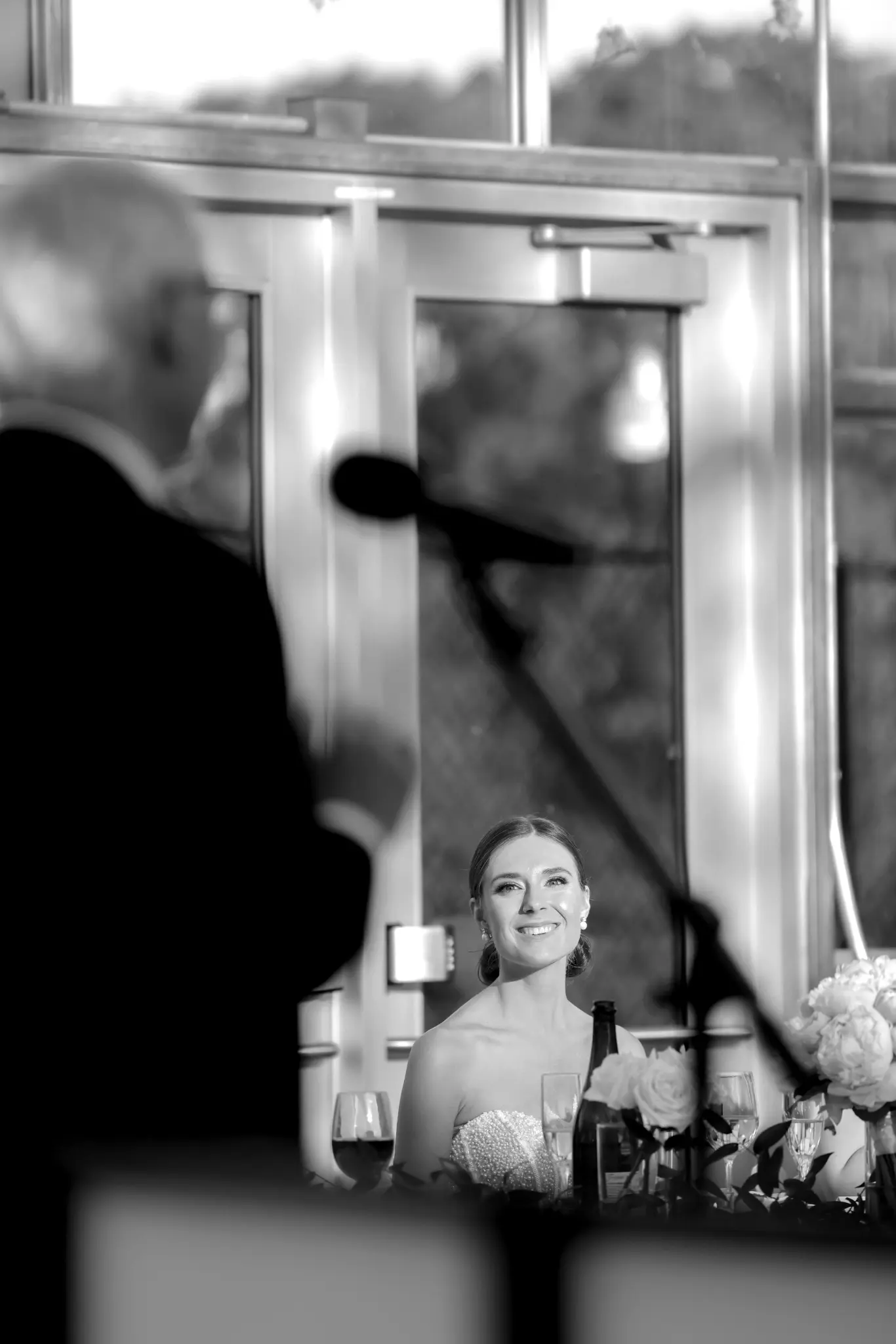 Black-and-white portrait of a bride viewed through glass during the wedding reception