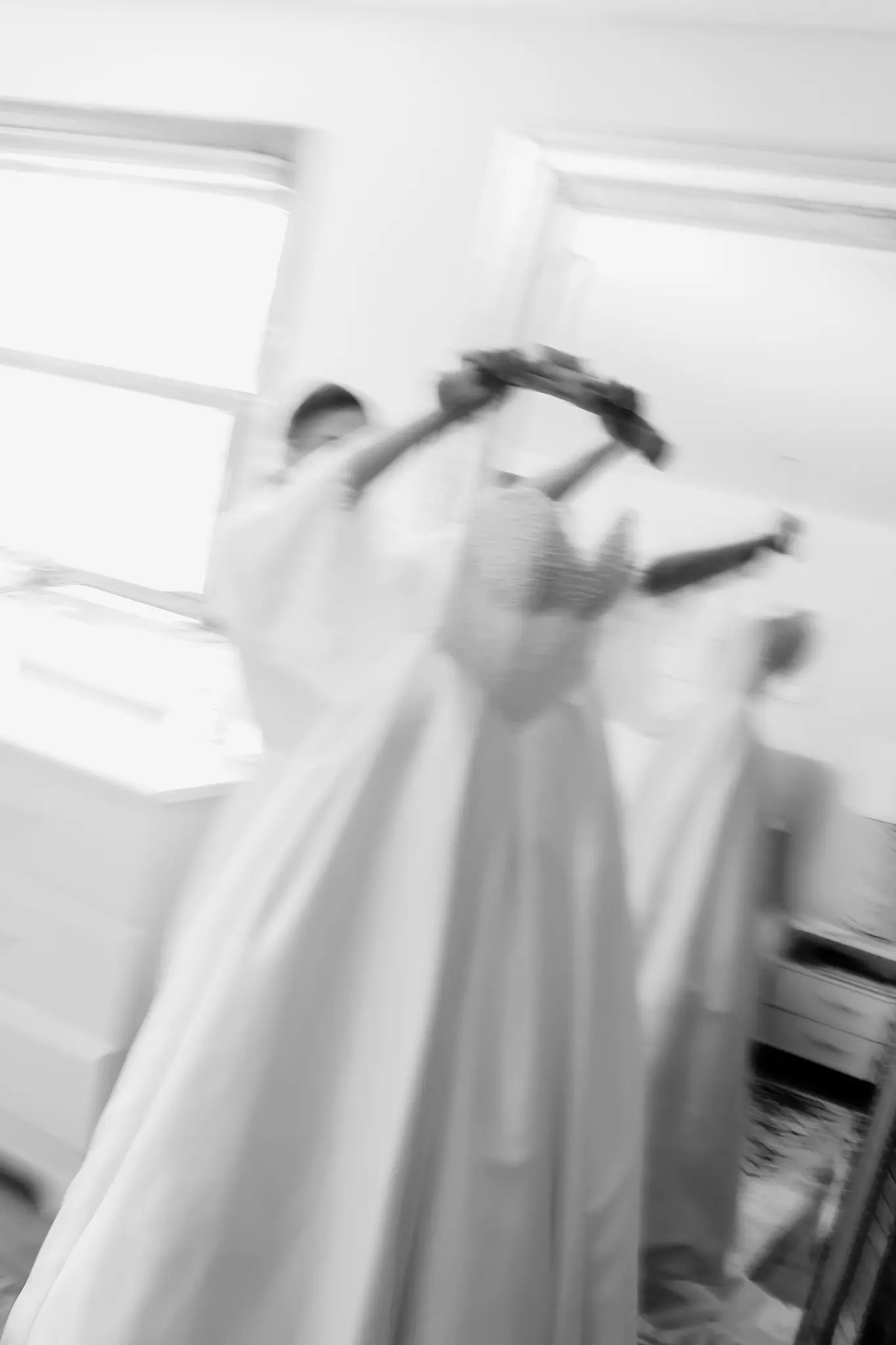 Black-and-white moment of attendants helping a bride into her wedding gown