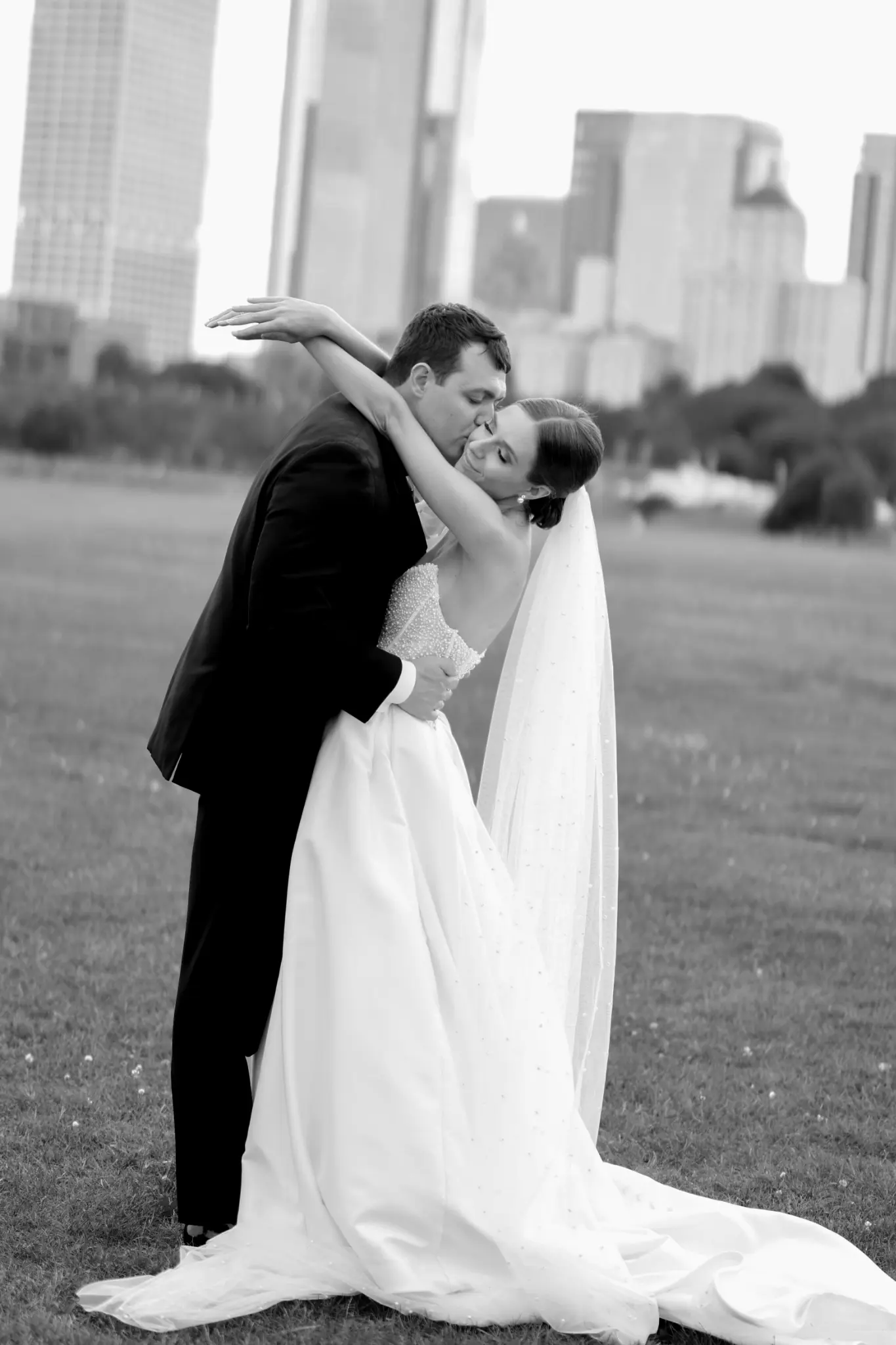 Black-and-white full-length wedding couple embrace in an open urban setting