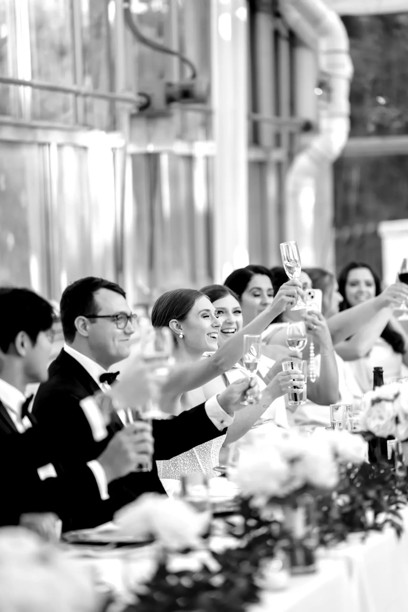 Black-and-white wedding guests raising glasses during a reception toast