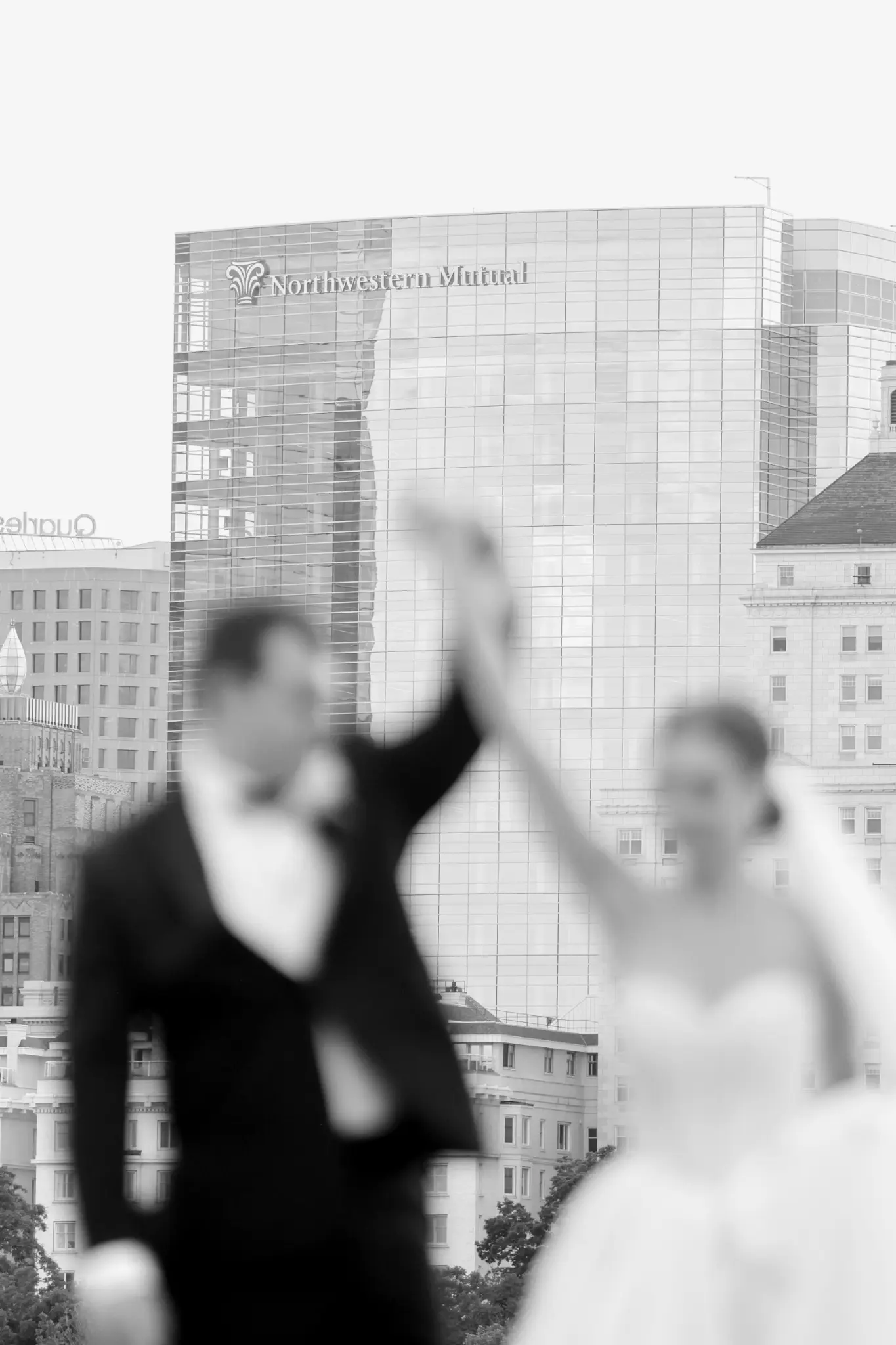 Soft-focus black-and-white wedding couple portrait with city architecture behind them