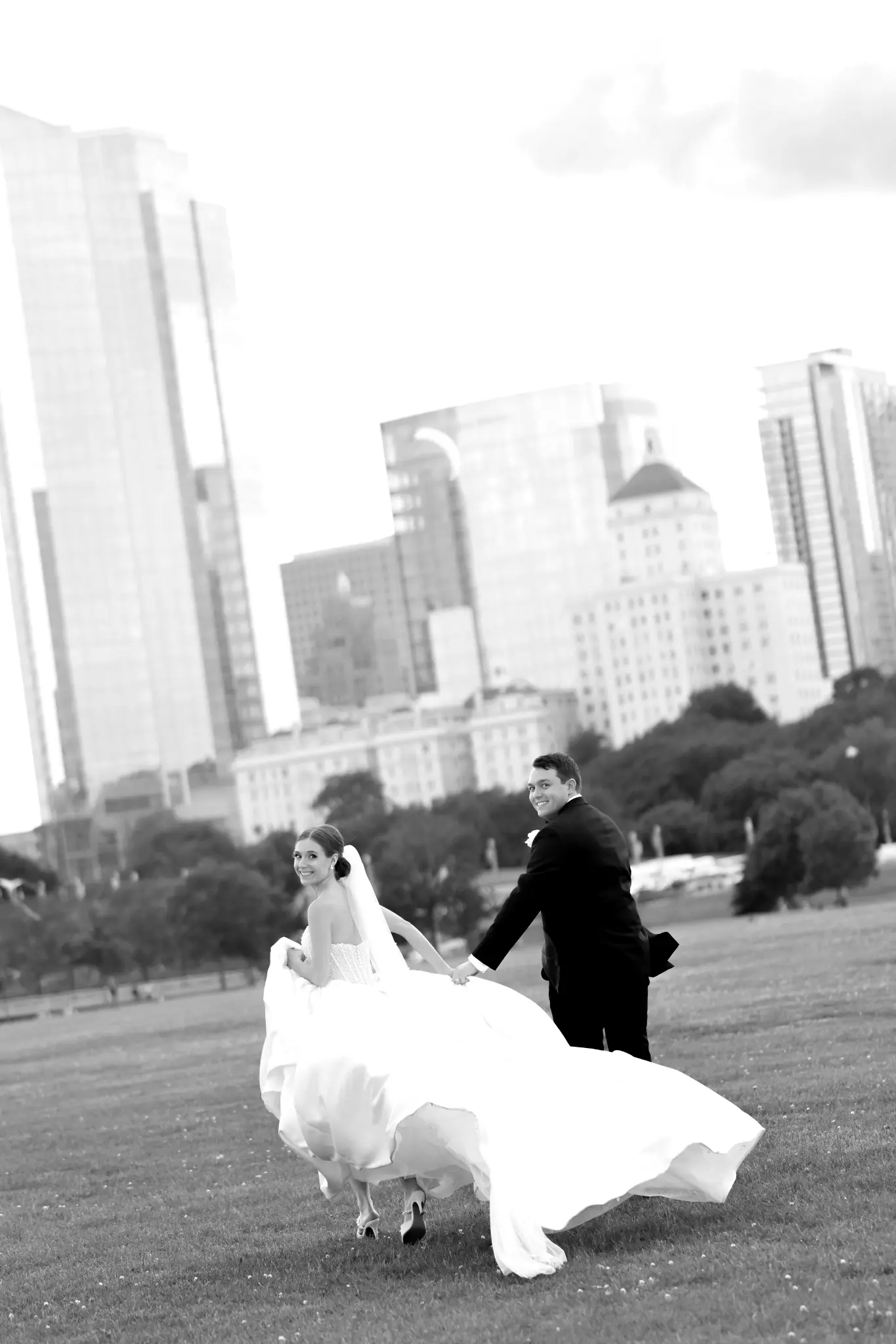 Bride and groom in formal attire in a city park with skyline beyond