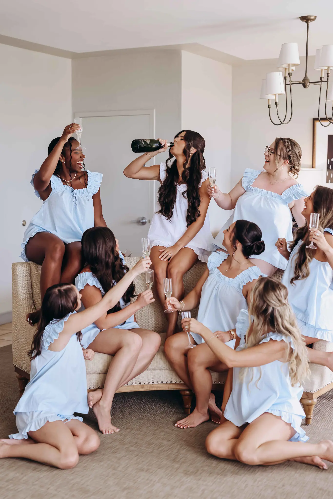 Bride celebrating with champagne and attendants in pale-blue outfits during wedding preparations
