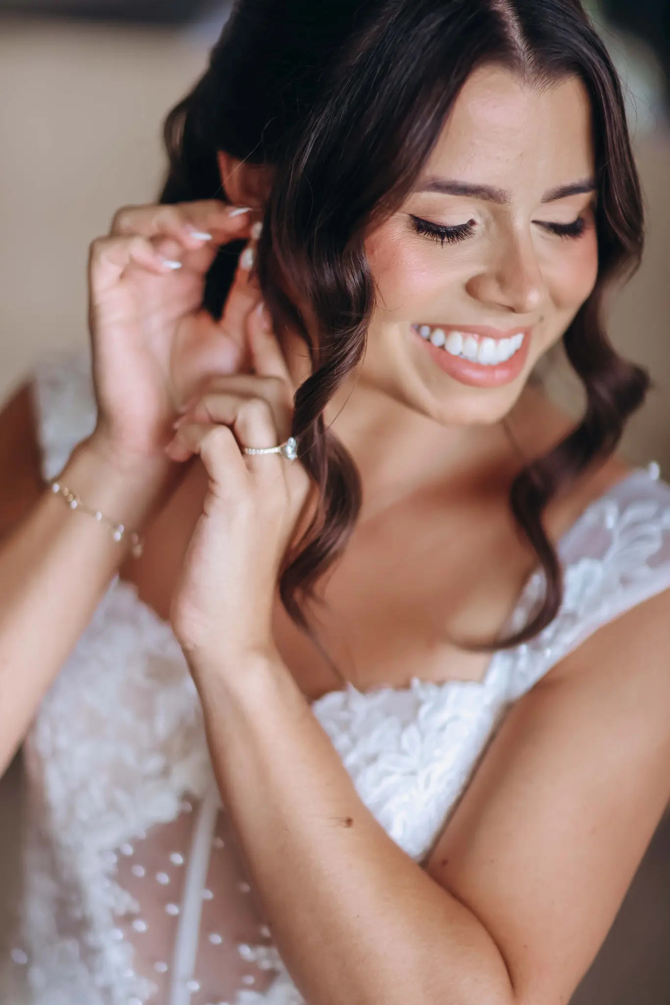 Bride smiling as she fastens an earring during wedding preparations